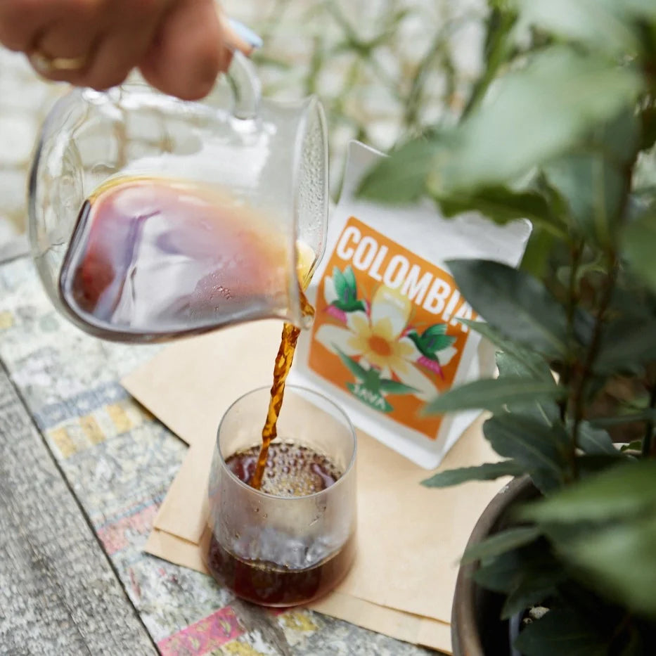 Nalewanie kawy z przelewu do szklanki – w tle opakowanie Colombia Tolima od JAVA Coffee Roasters i zielone liście rośliny