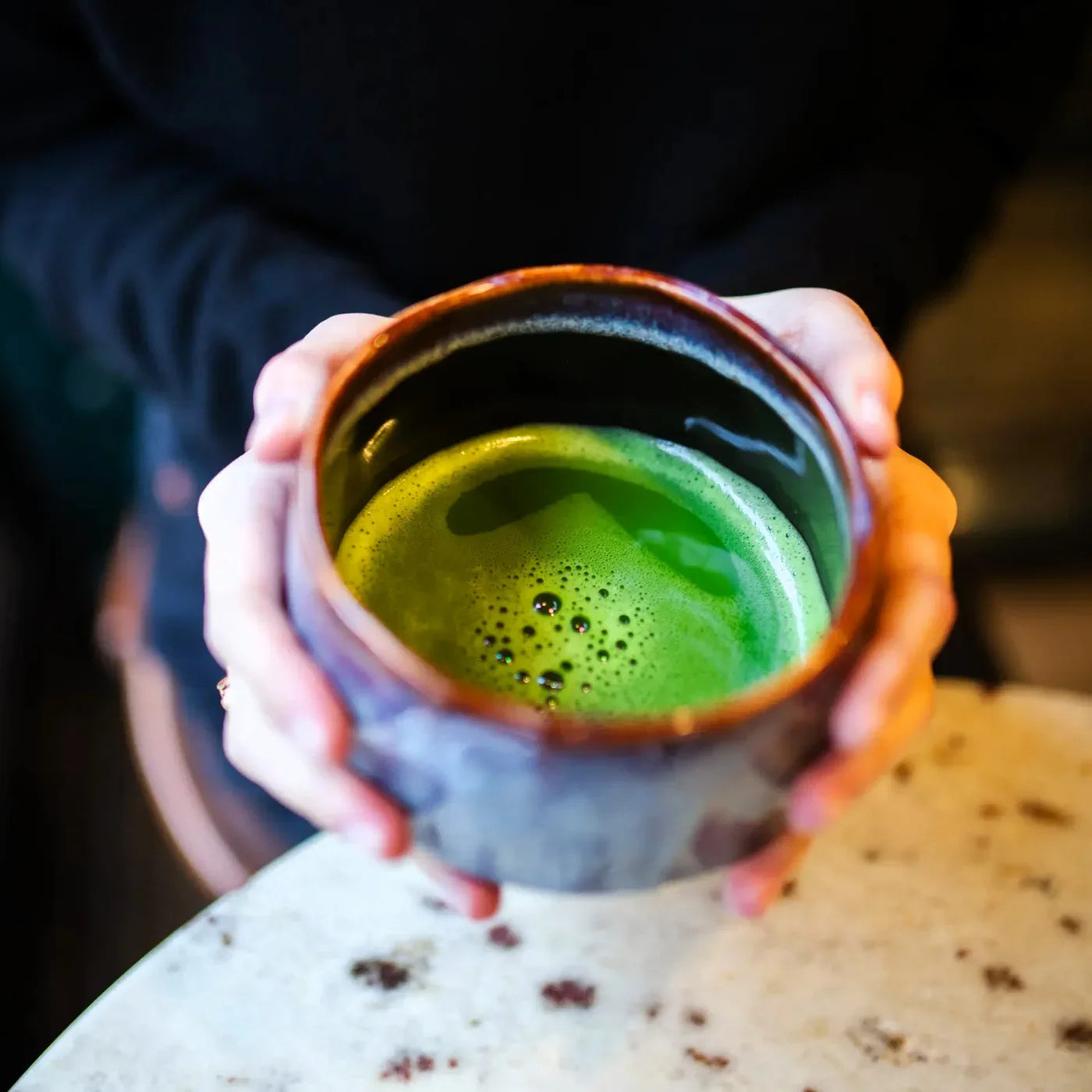 Ceramiczna czarka do matchy z gęstą, zieloną matchą trzymana w dłoniach, ręcznie wykonana miseczka w klimatycznym wnętrzu.