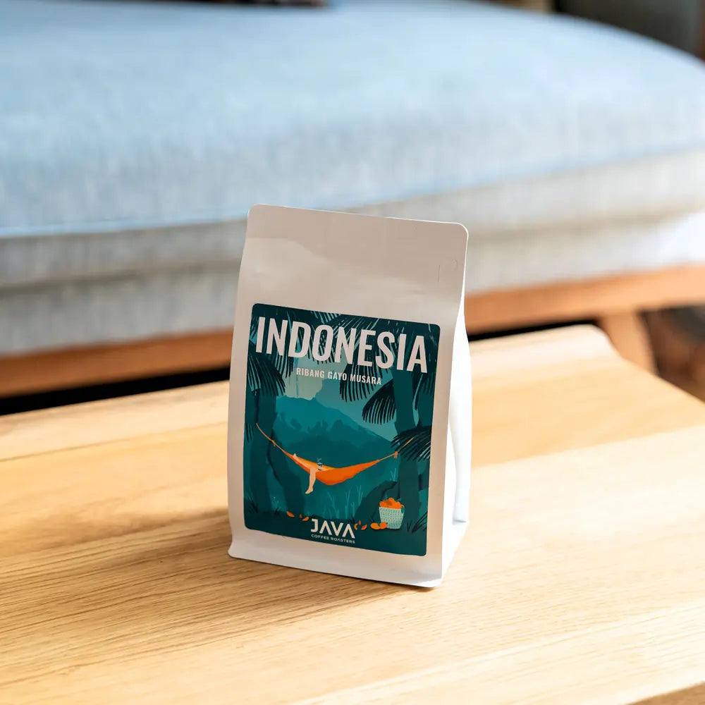 Kawa specialty Indonesia Ribang Gayo Musara od JAVA Coffee Roasters w białym opakowaniu na drewnianym stoliku