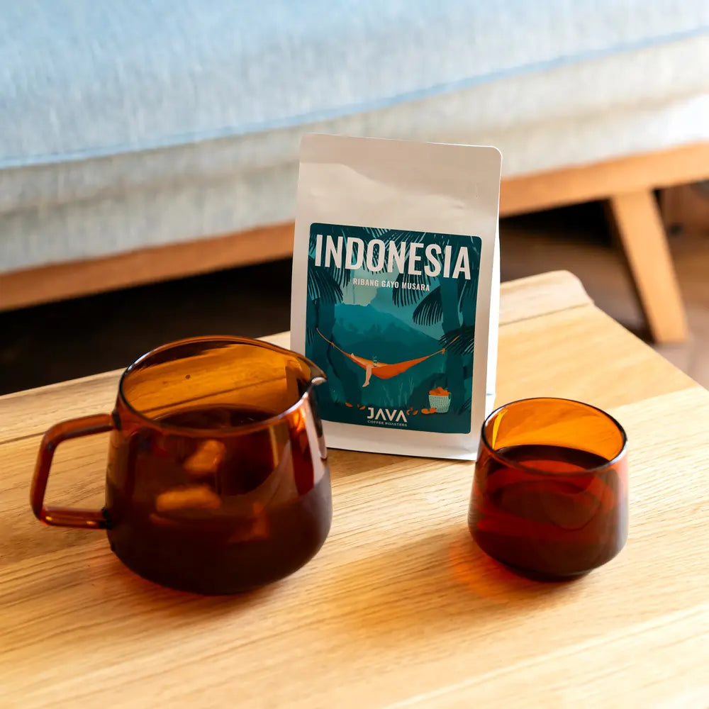 Kawa specialty Indonesia Ribang Gayo Musara od JAVA Coffee Roasters z zaparzoną kawą w bursztynowych naczyniach na drewnianym stoliku