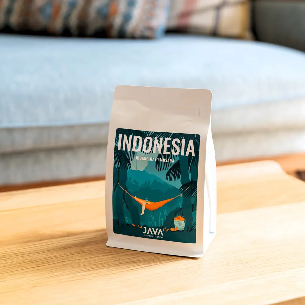 Kawa specialty Indonesia Ribang Gayo Musara od JAVA Coffee Roasters w białym opakowaniu na drewnianym stoliku