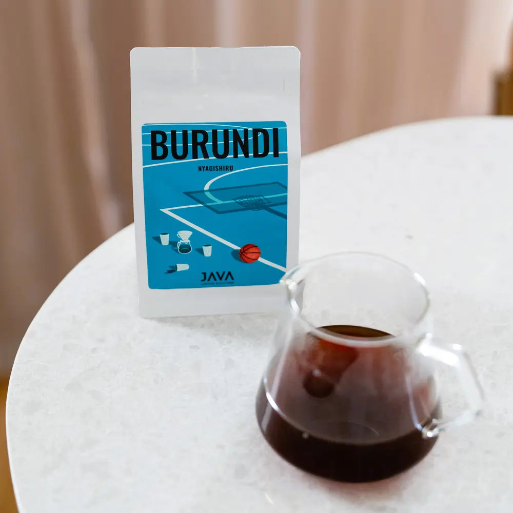 Opakowanie kawy Burundi Nyagishiru od JAVA Coffee Roasters na stole obok szklanego dzbanka z zaparzoną kawą filtrową