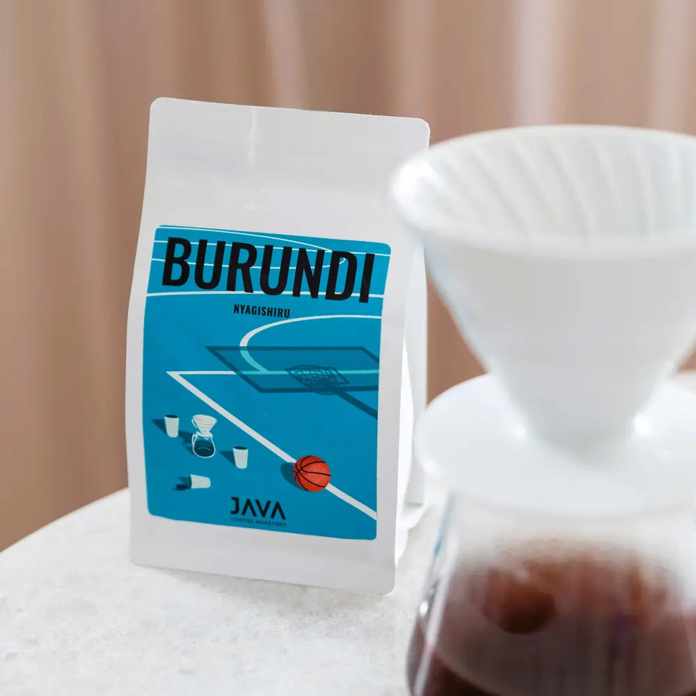 Kawa Burundi Nyagishiru od JAVA Coffee Roasters w białym opakowaniu z niebieską etykietą, obok drippera i dzbanka do przelewu