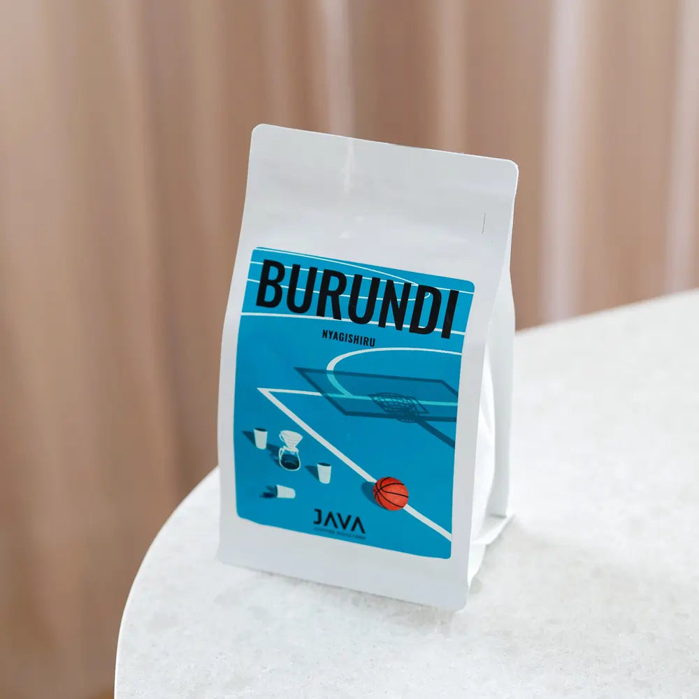 Opakowanie kawy Burundi Nyagishiru od JAVA Coffee Roasters w białej paczce z niebieską etykietą na tle jasnego stołu