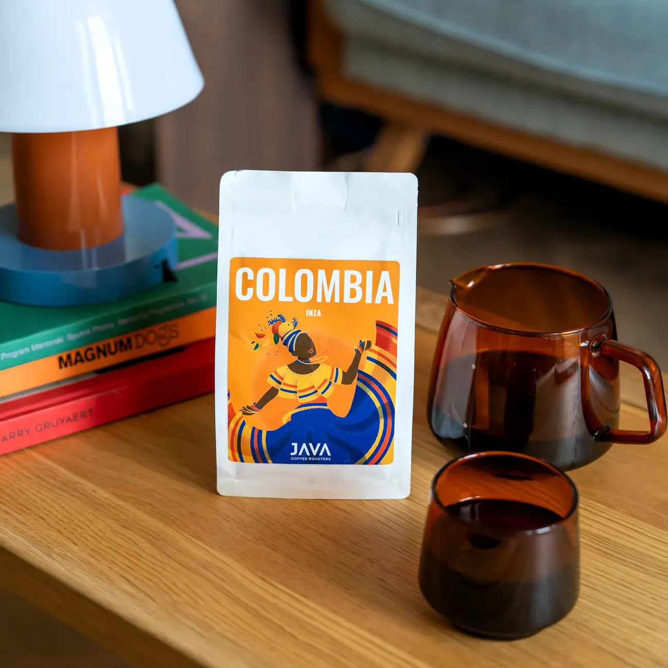Kawa Java Coffee Colombia Inza – paczka kawy specialty na stole obok szklanego dzbanka i filiżanki w kolorze bursztynowym