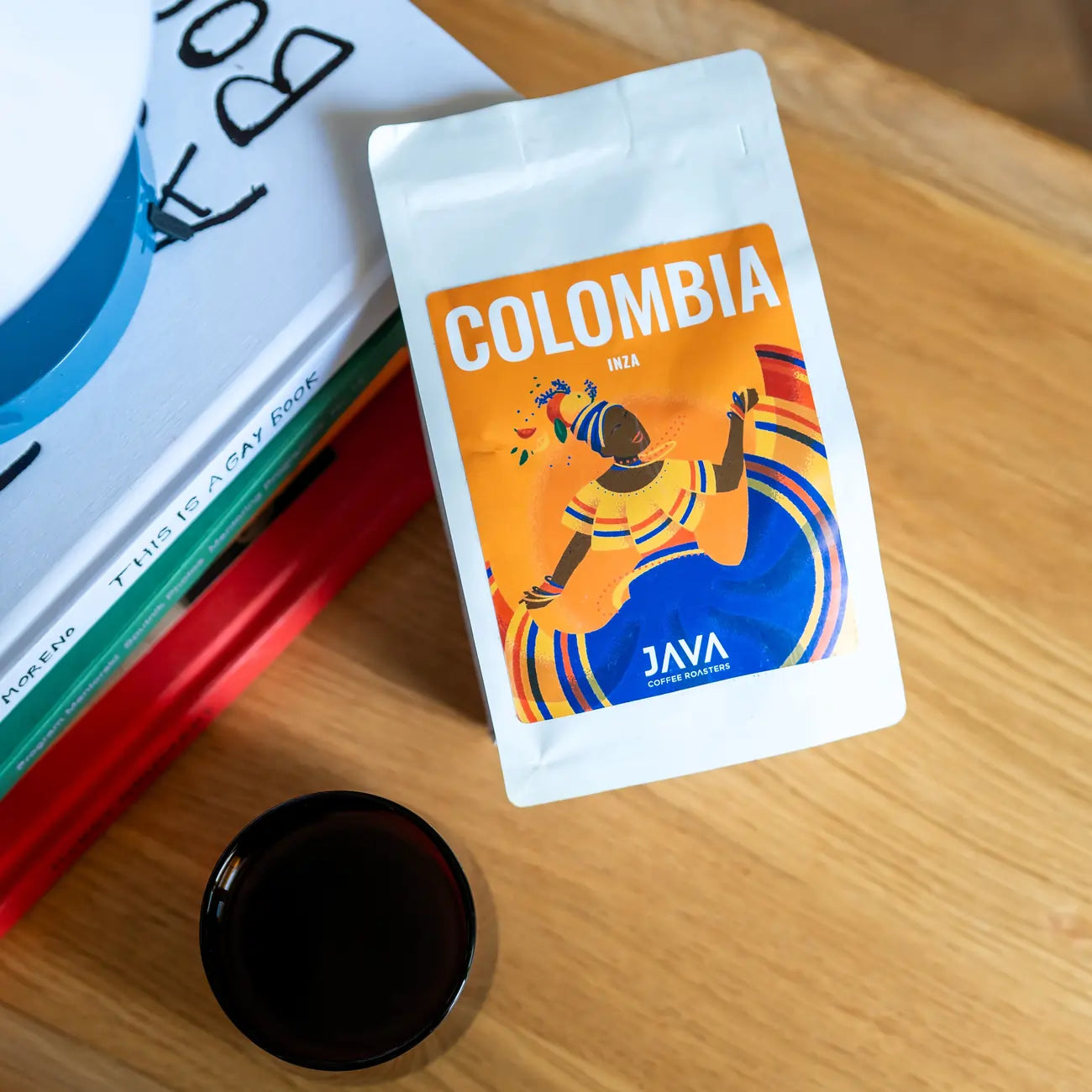 Kawa Java Coffee Colombia Inza – paczka kawy specialty na stole obok książek i filiżanki z czarną kawą