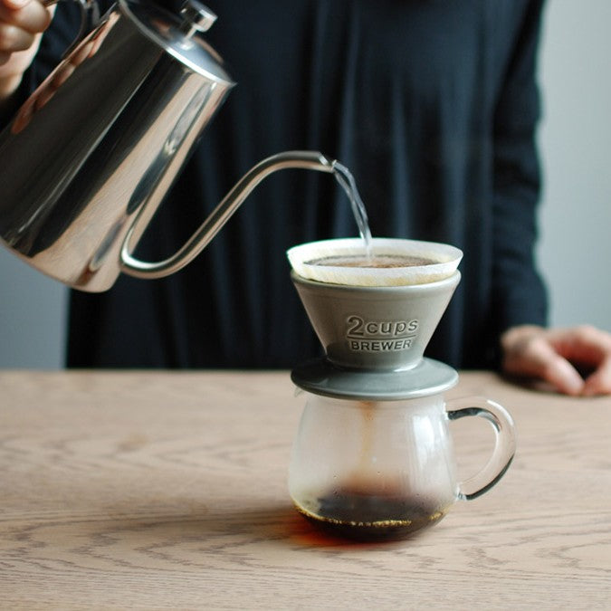 Parzenie kawy metodą pour-over z użyciem ceramicznego drippera KINTO i szklanego serwera na drewnianym stole.