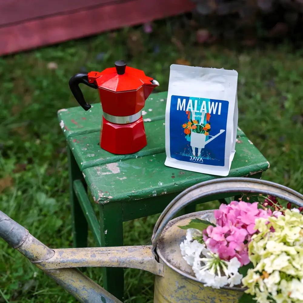 Kawa Malawi Ngapani od JAVA Coffee Roasters na zielonym stoliku obok czerwonej kawiarki moka – idealna propozycja kawy specialty dla gastronomii i biur.