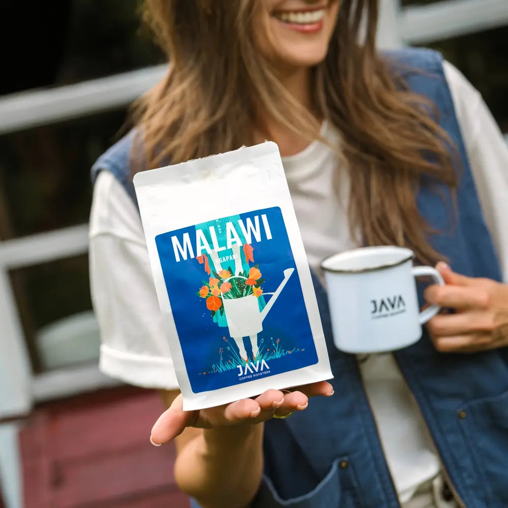 Opakowanie kawy Malawi Ngapani od JAVA Coffee Roasters trzymane w dłoni obok kubka z logo JAVA – propozycja kawy specialty dla biznesu.