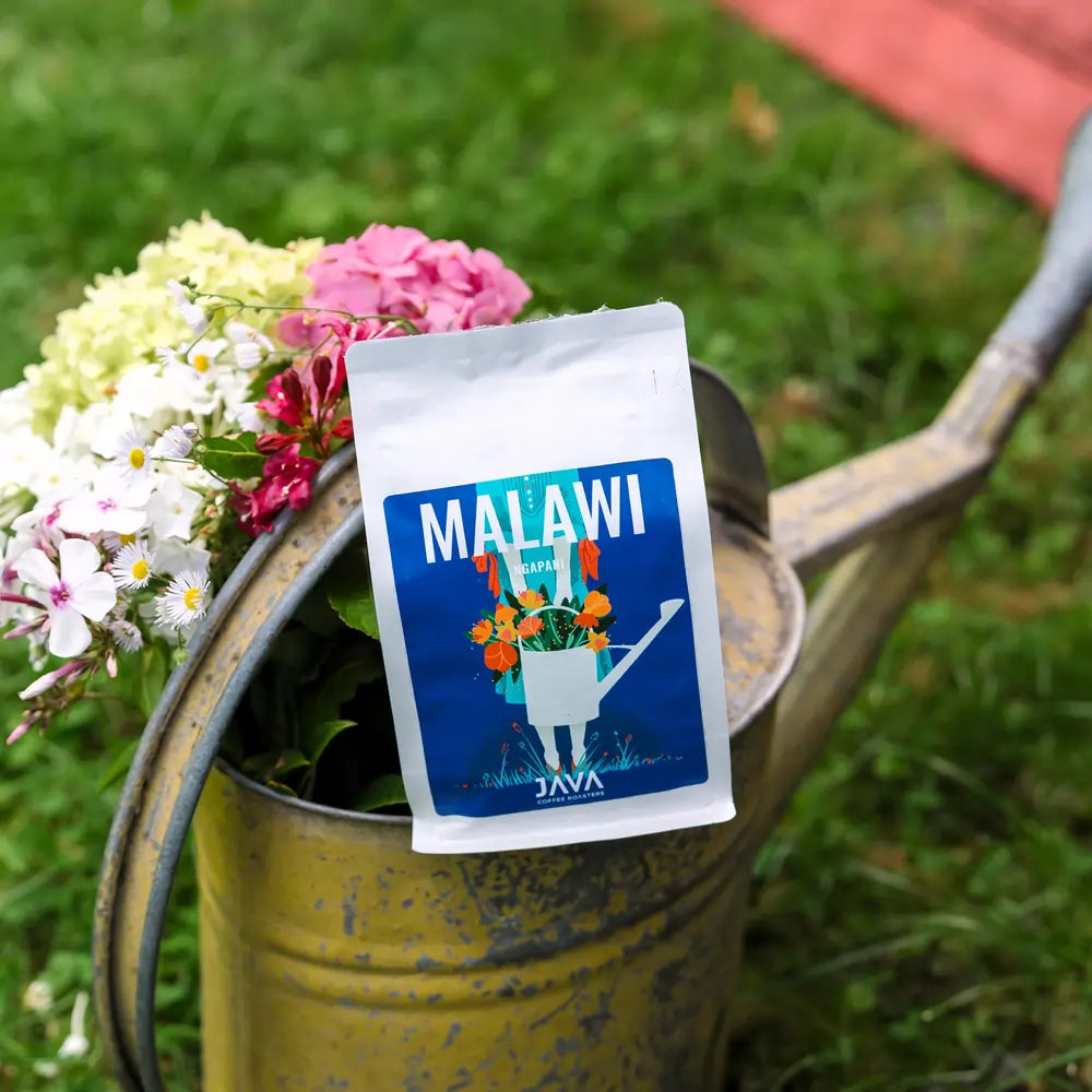 Opakowanie kawy Malawi Ngapani od JAVA Coffee Roasters oparte o żółtą konewkę z kwiatami – propozycja kawy specialty dla biur, kawiarni i gastronomii.