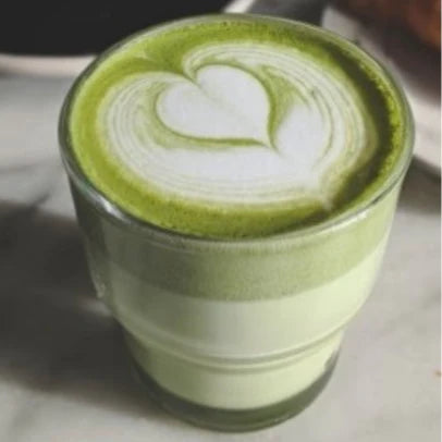 Szklanka matcha latte z pięknym wzorem serca wykonanym w technice latte art, ustawiona na stole.