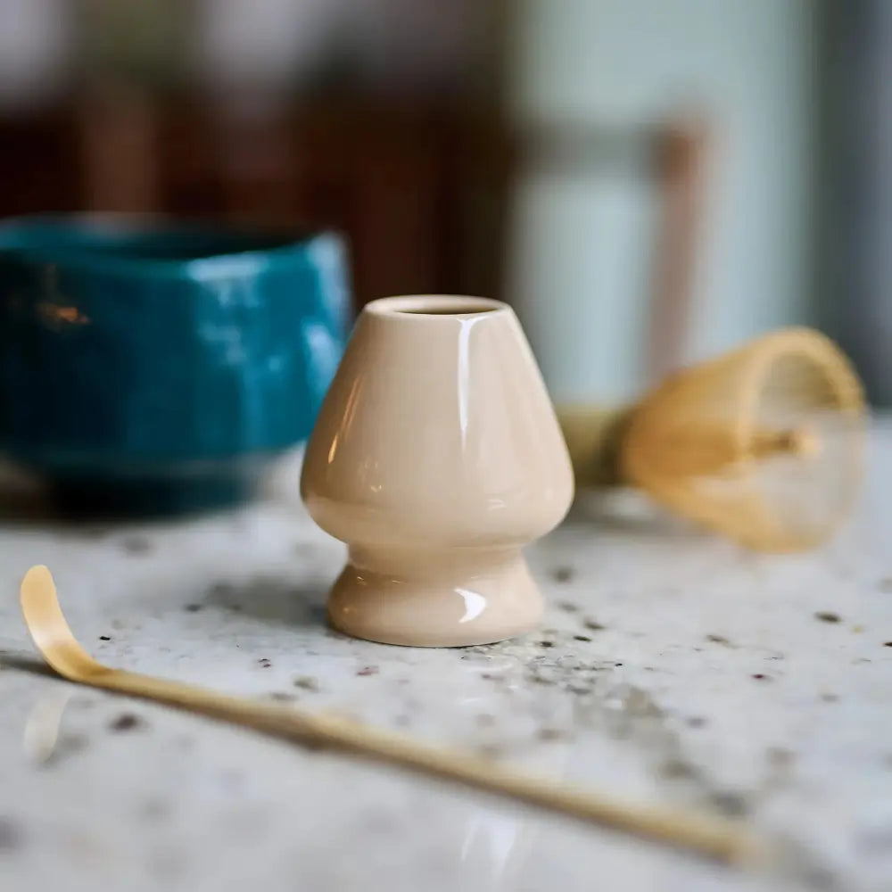 Beżowa podstawka na chasen (naoshi) z porcelany – akcesorium do matchy w tradycyjnym japońskim stylu, na marmurowym blacie z miotełką w tle