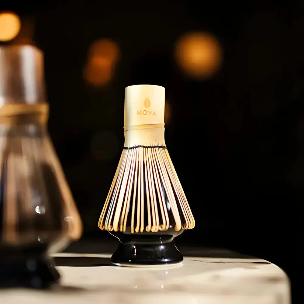 Czarna porcelanowa podstawka na chasen (naoshi) z bambusową miotełką Moya – eleganckie akcesorium do matchy na tle ciemnego wnętrza