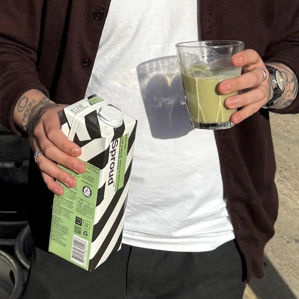 Osoba trzymająca szklankę z napojem Sproud Matcha i karton napoju roślinnego w dłoniach w słoneczny dzień