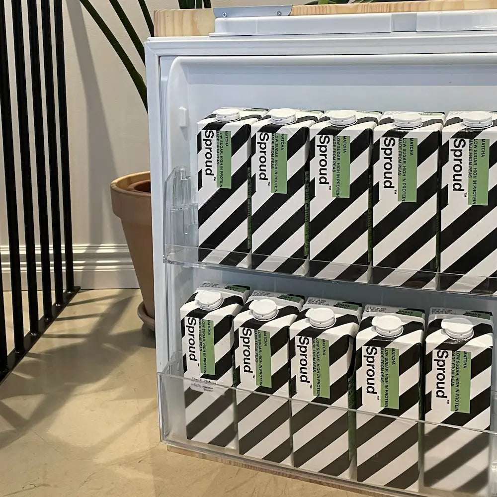 Kartonowe opakowania napoju roślinnego Sproud Matcha ułożone na półkach lodówki w jasnym wnętrzu