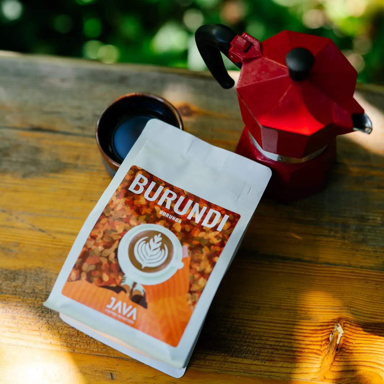 Opakowanie kawy specialty Burundi Burunga od JAVA Coffee Roasters obok czerwonej kawiarki i filiżanki czarnej kawy.