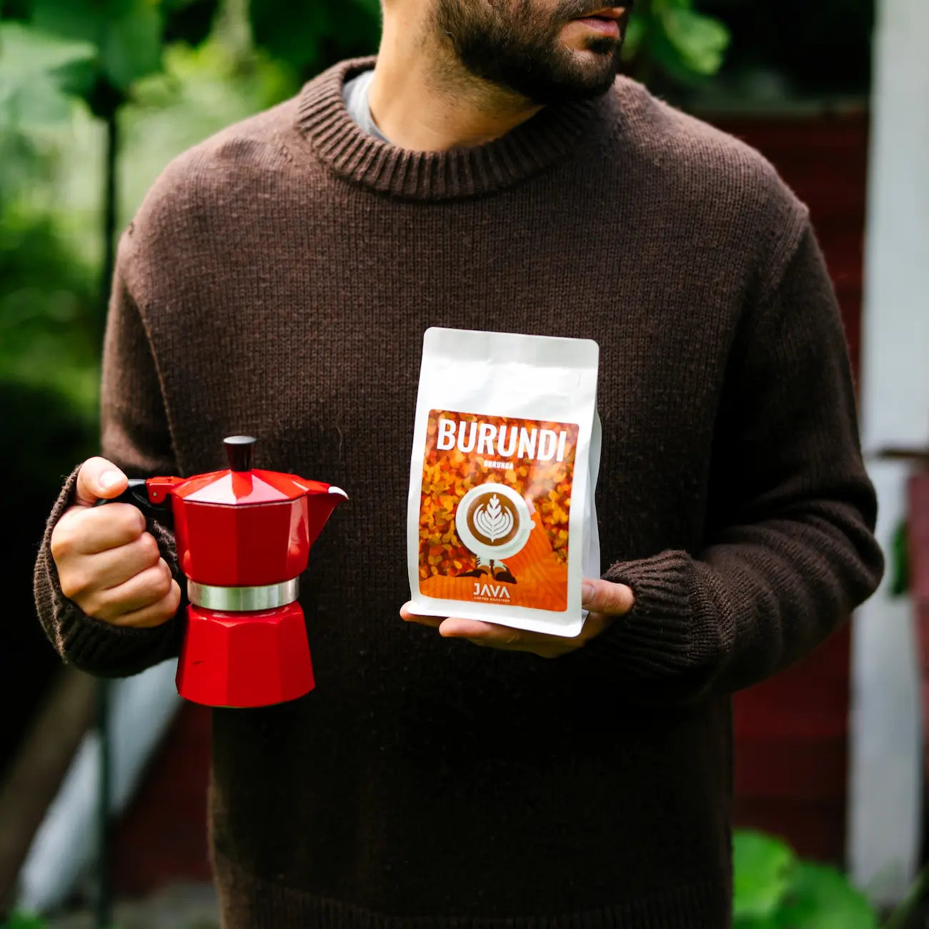 Mężczyzna trzymający opakowanie kawy ziarnistej specialty Burundi Burunga od JAVA Coffee Roasters oraz czerwoną kawiarkę do domowego parzenia kawy.