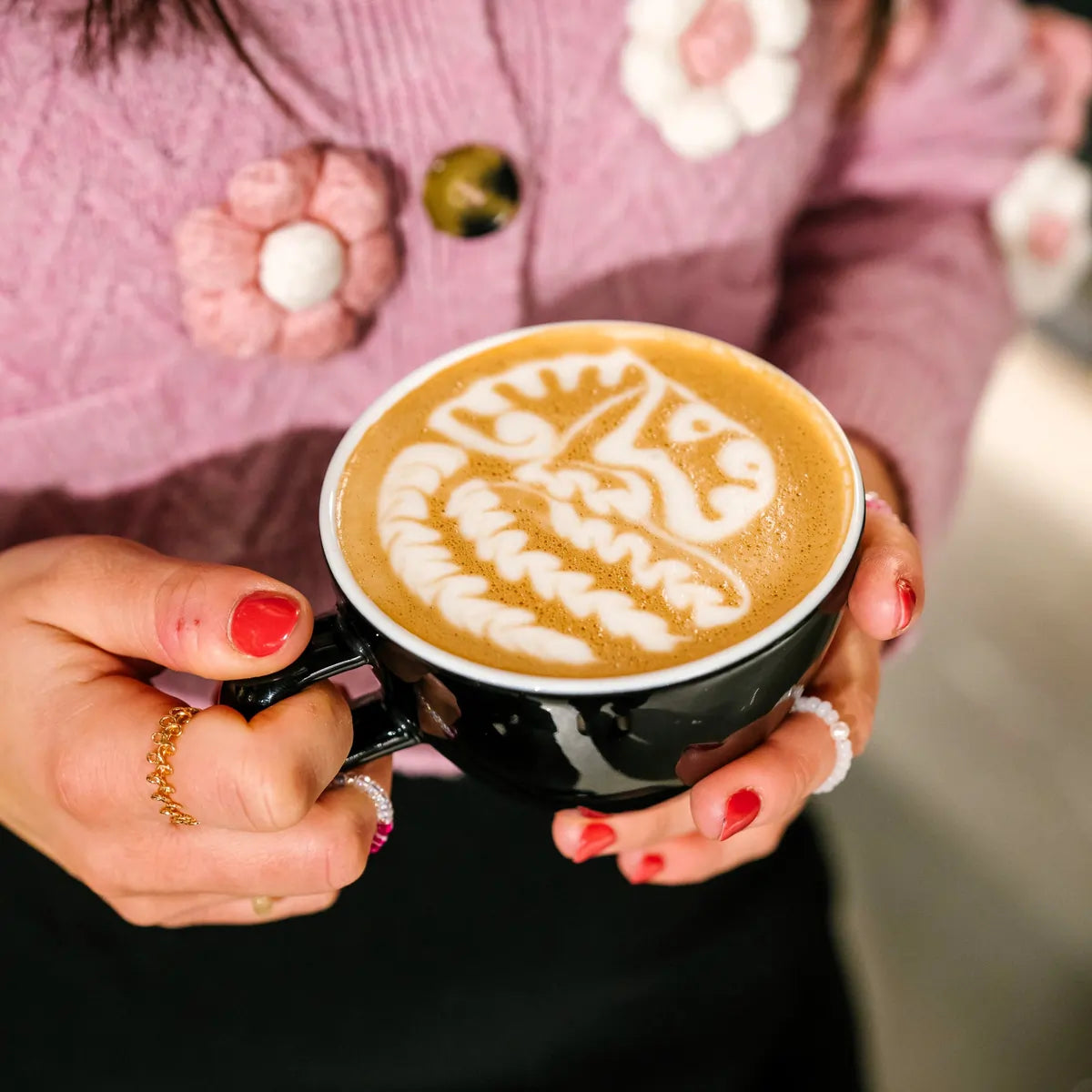 Cappuccino z latte artem trzymane w dłoniach, kawa specialty JAVA Coffee – zdjęcie lifestyle w kawiarni