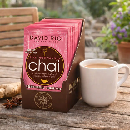 Flamingo Vanilla Chai David Rio – bezkofeinowe i bezcukrowe saszetki chai w ekspozytorze obok filiżanki chai latte, relaks na świeżym powietrzu