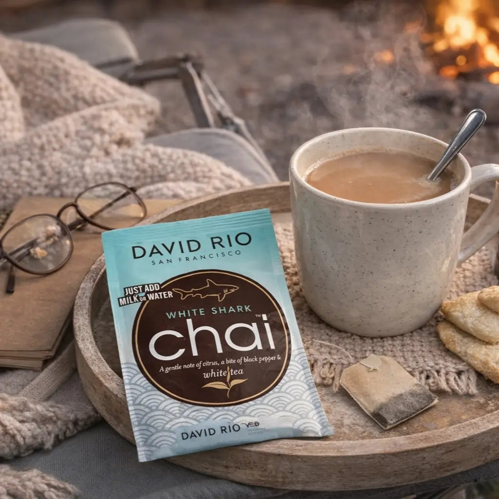 White Shark Chai David Rio – delikatne chai latte z białej herbaty w saszetce, podane w filiżance obok herbaty i ciastek, przytulny domowy klimat przy kominku