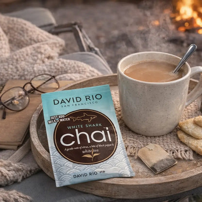 White Shark Chai David Rio – delikatne chai latte z białej herbaty w saszetce, podane w filiżance obok herbaty i ciastek, przytulny domowy klimat przy kominku