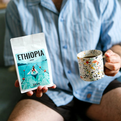 Osoba trzymająca opakowanie etiopskiej kawy specialty Ethiopia Konga od JAVA Coffee Roasters oraz kubek z zaparzoną kawą.