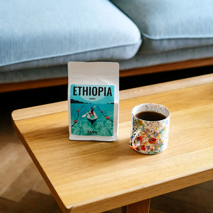 Opakowanie etiopskiej kawy specialty Ethiopia Konga od JAVA Coffee Roasters obok kubka z czarną kawą na drewnianym stole.