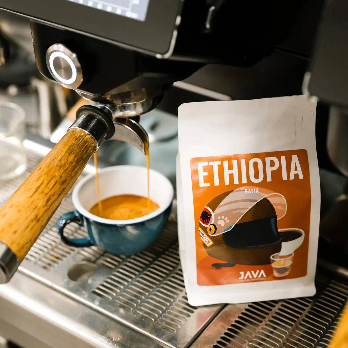 Parzenie espresso z kawy Etiopia Gatta – opakowanie JAVA Coffee Roasters obok filiżanki pod kolbą ekspresu ciśnieniowego