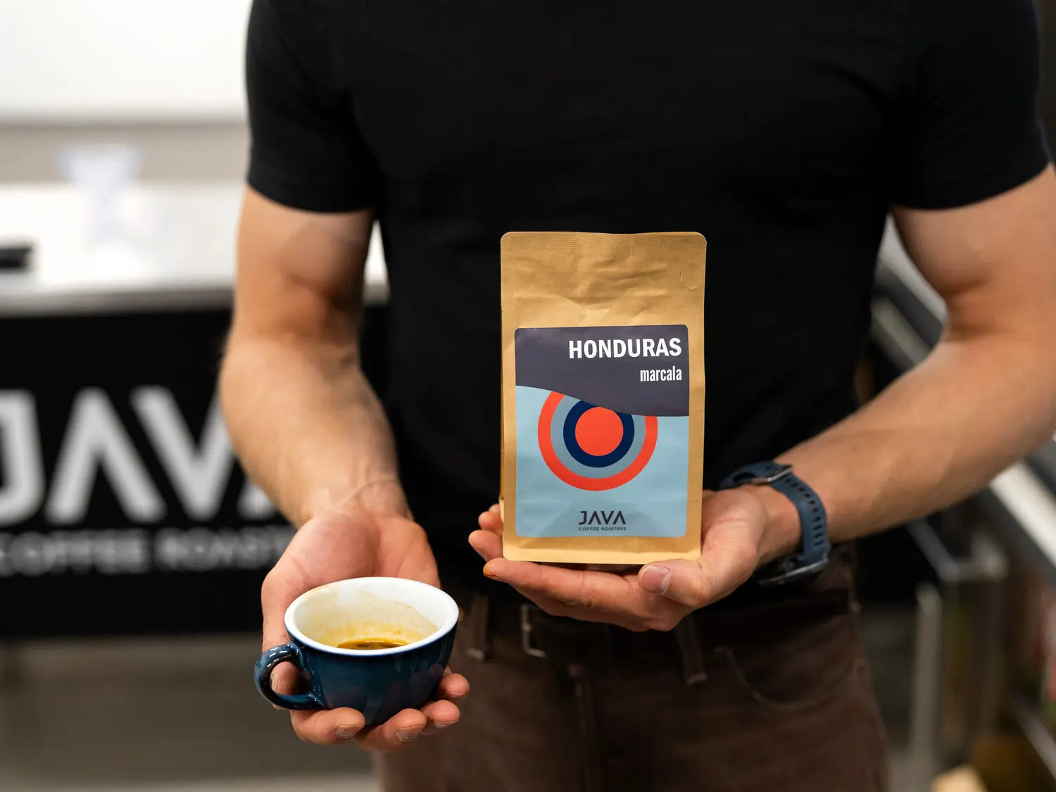 Barista prezentujący kawę specialty Honduras Marcala od JAVA Coffee Roasters oraz filiżankę espresso w palarni kawy.