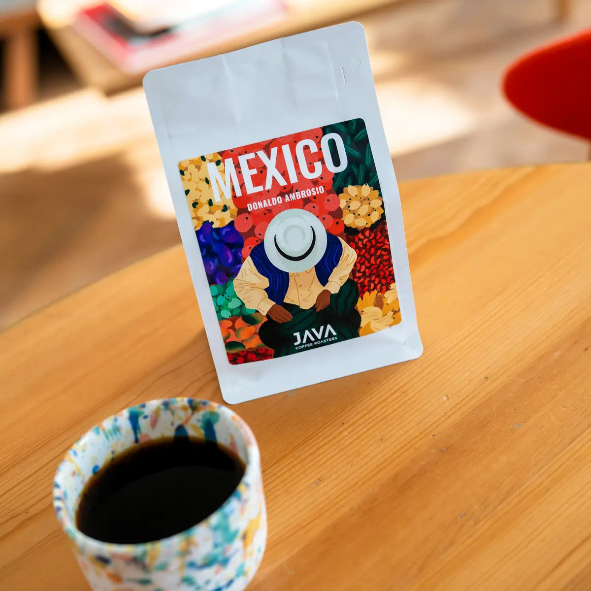 Kawa specialty Mexico Donaldo Ambrosio od JAVA Coffee Roasters – opakowanie kawy do metod przelewowych na drewnianym stole, na pierwszym planie filiżanka czarnej kawy, zdjęcie lifestyle.