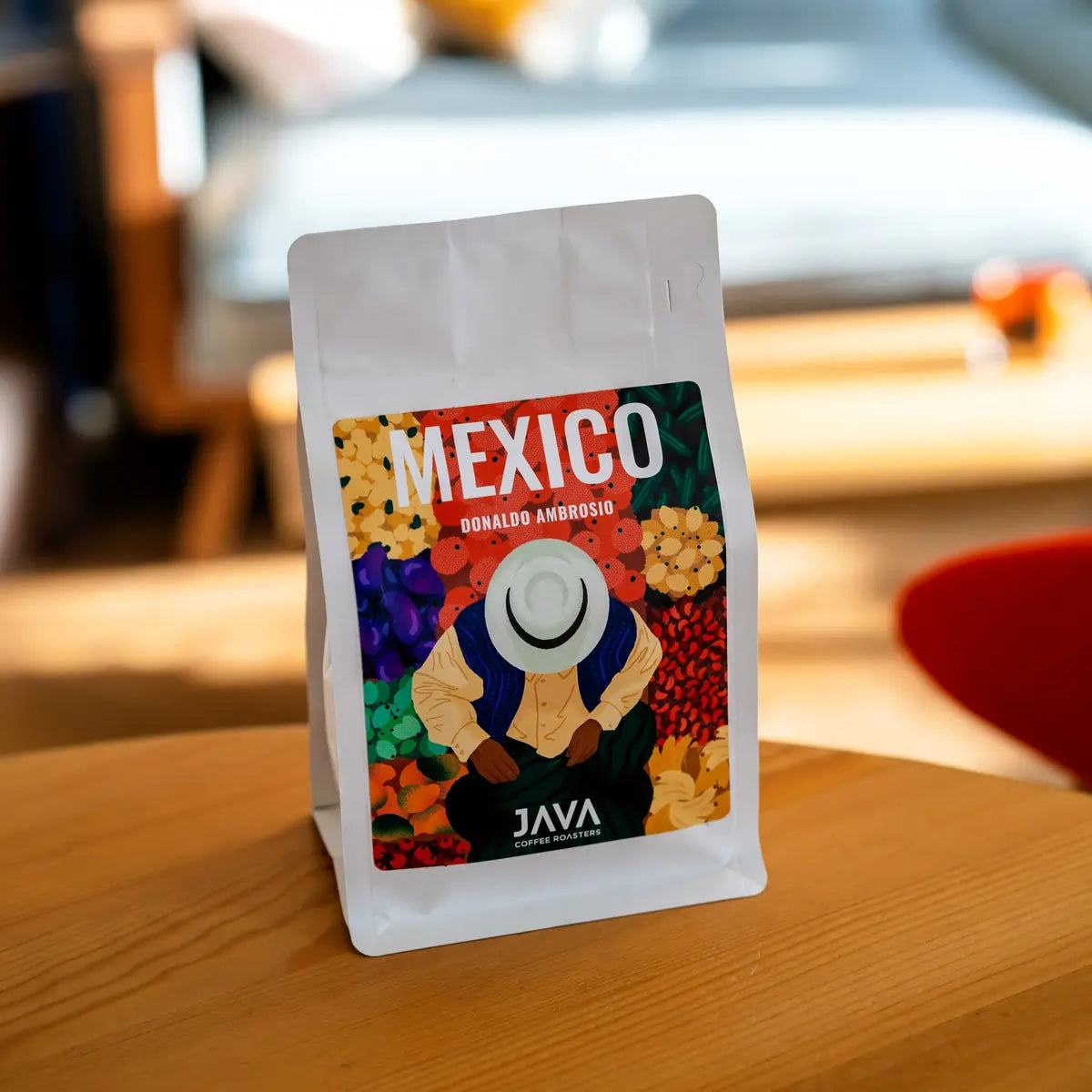 Opakowanie kawy specialty Mexico Donaldo Ambrosio od JAVA Coffee Roasters ustawione na drewnianym stole, zdjęcie lifestyle we wnętrzu kawowym.