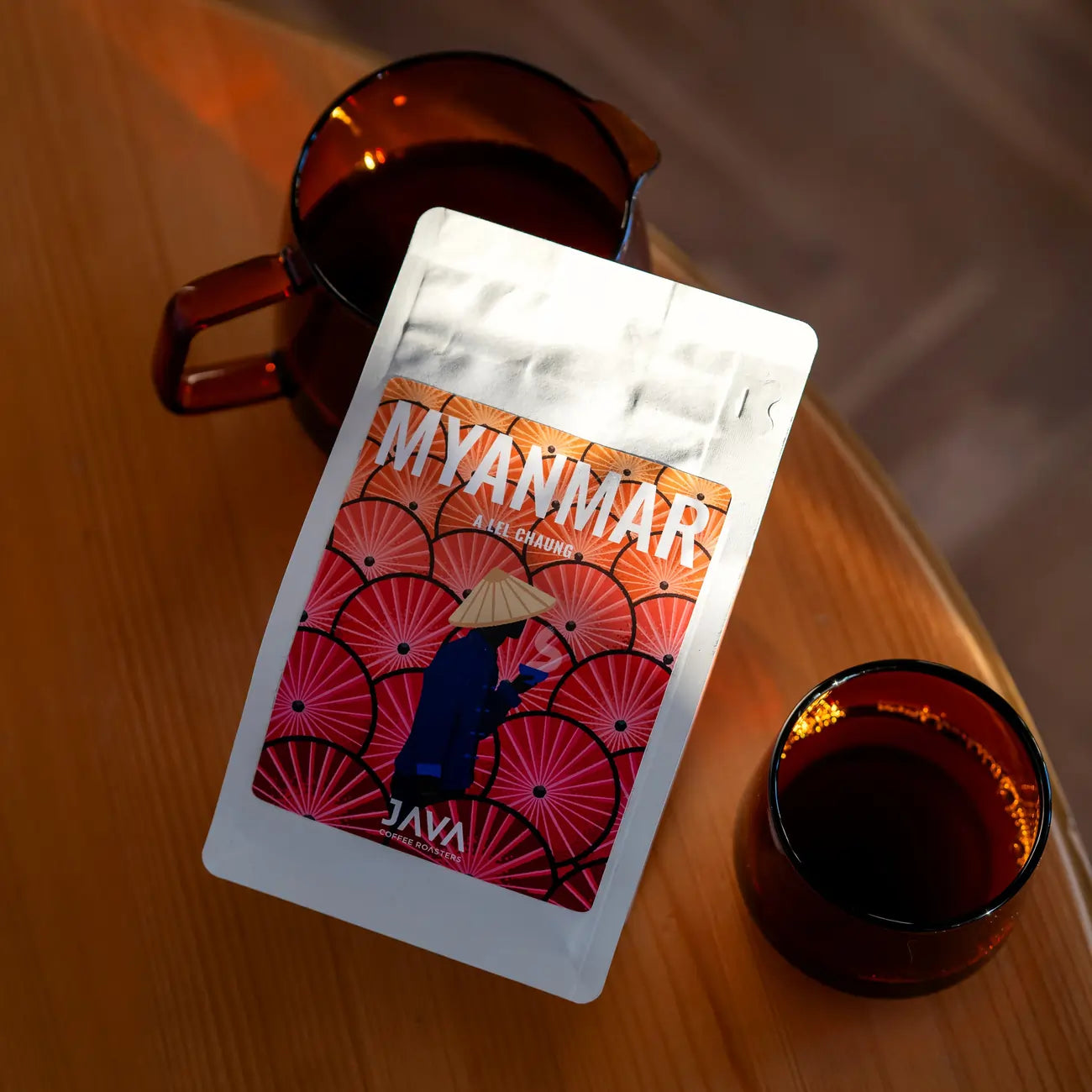 Flat lay opakowania kawy JAVA Coffee Roasters Myanmar A Lei Chaung z dzbankiem i filiżanką na drewnianym stole