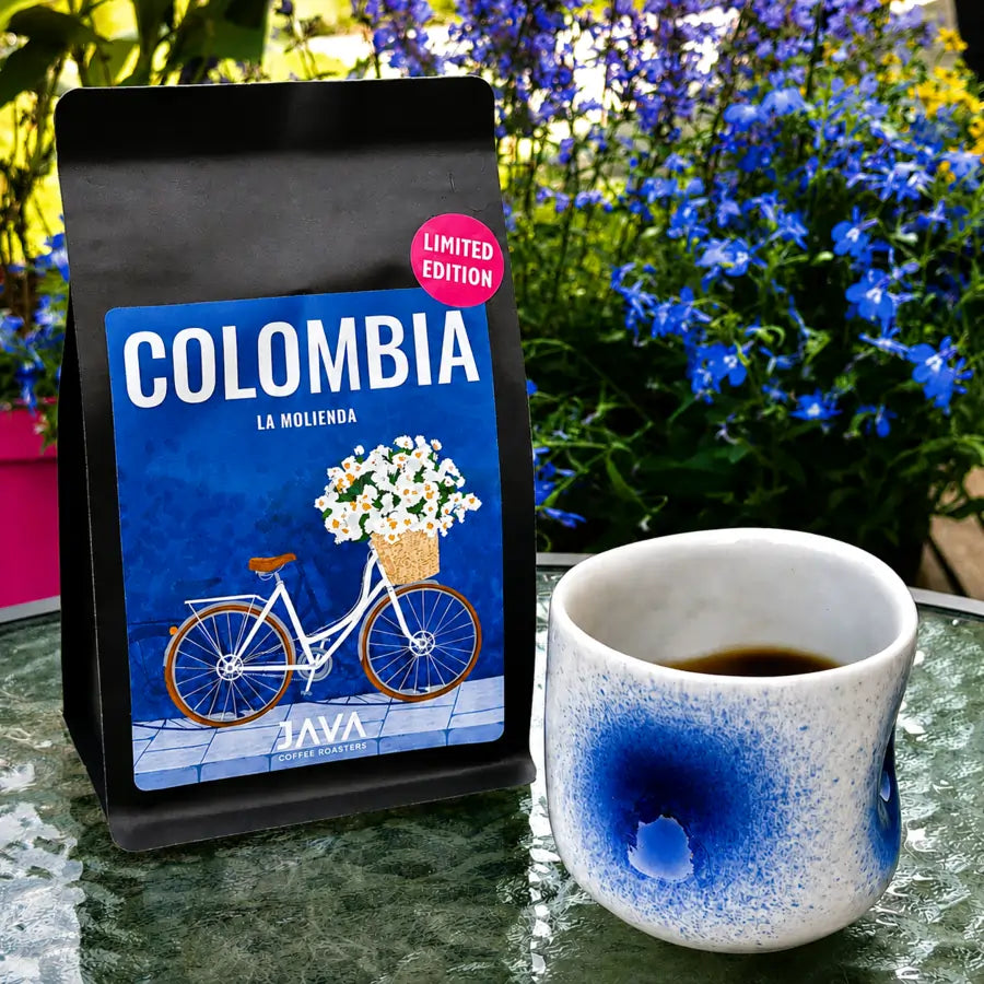 Opakowanie kawy ziarnistej Colombia La Molienda JAVA Coffee obok filiżanki czarnej kawy na szklanym stoliku w ogrodzie.