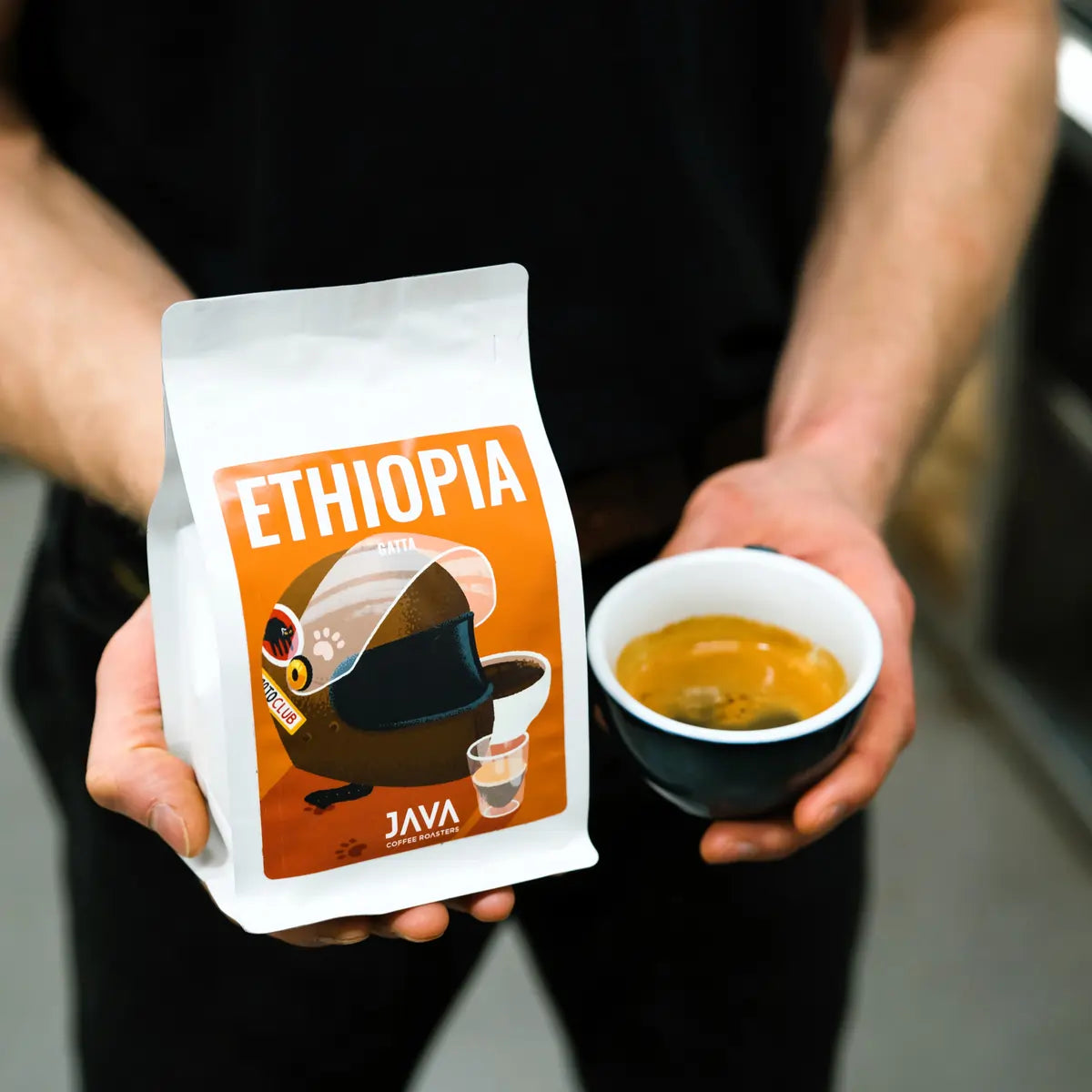 Kawa Ethiopia Gatta od JAVA Coffee Roasters trzymana w dłoniach obok filiżanki espresso – zdjęcie lifestyle baristyczne