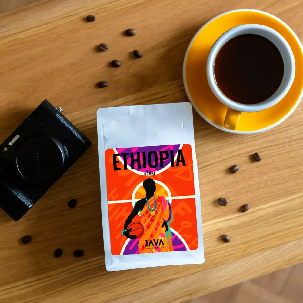 Kawa specialty Java Ethiopia Bombe 250 g na stole obok filiżanki kawy i aparatu – ujęcie lifestyle