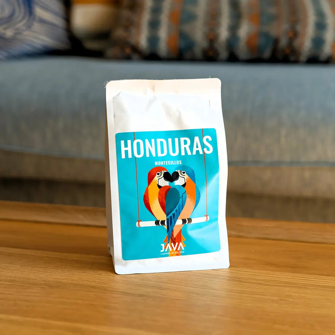 Kawa Java Honduras Montecillos 250g w białym opakowaniu stojąca na drewnianym stole, ujęcie lifestyle w domowym wnętrzu