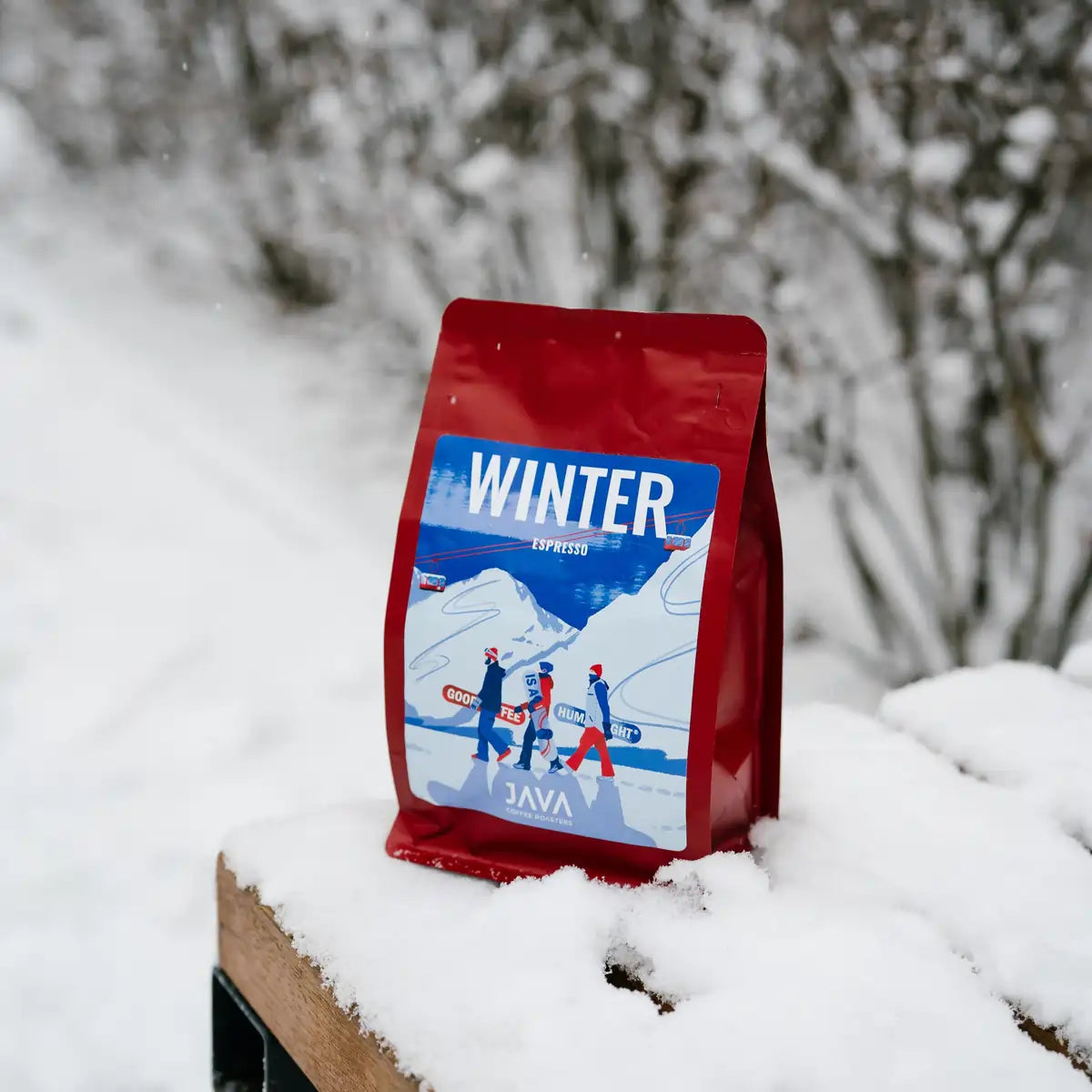 Opakowanie kawy JAVA Coffee Winter Espresso w czerwonej torbie ustawione na śniegu w zimowym otoczeniu.