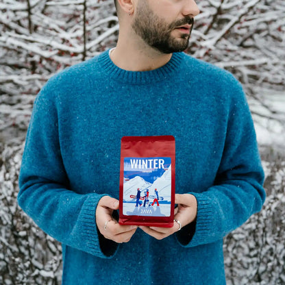 Mężczyzna trzyma czerwone opakowanie kawy JAVA Coffee Winter Espresso w zimowym otoczeniu.