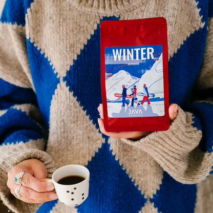 Osoba trzyma czerwone opakowanie kawy JAVA Coffee Winter Espresso oraz filiżankę z czarną kawą.