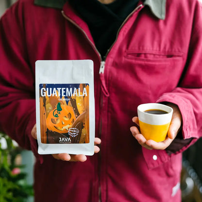Kawa specialty Guatemala Las Brisas JAVA Coffee Roasters 250g – opakowanie halloweenowe trzymane obok filiżanki kawy