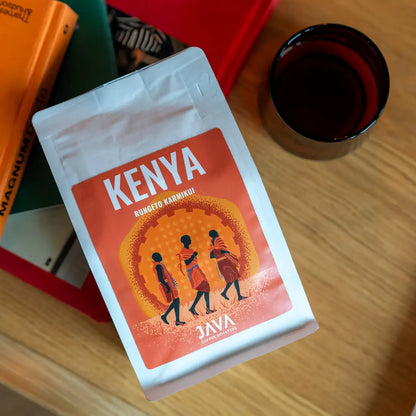 Kawa ziarnista Kenya Rungeto Karimikui JAVA Coffee Roasters położona na stole obok książek i szklanki z kawą, zdjęcie lifestyle