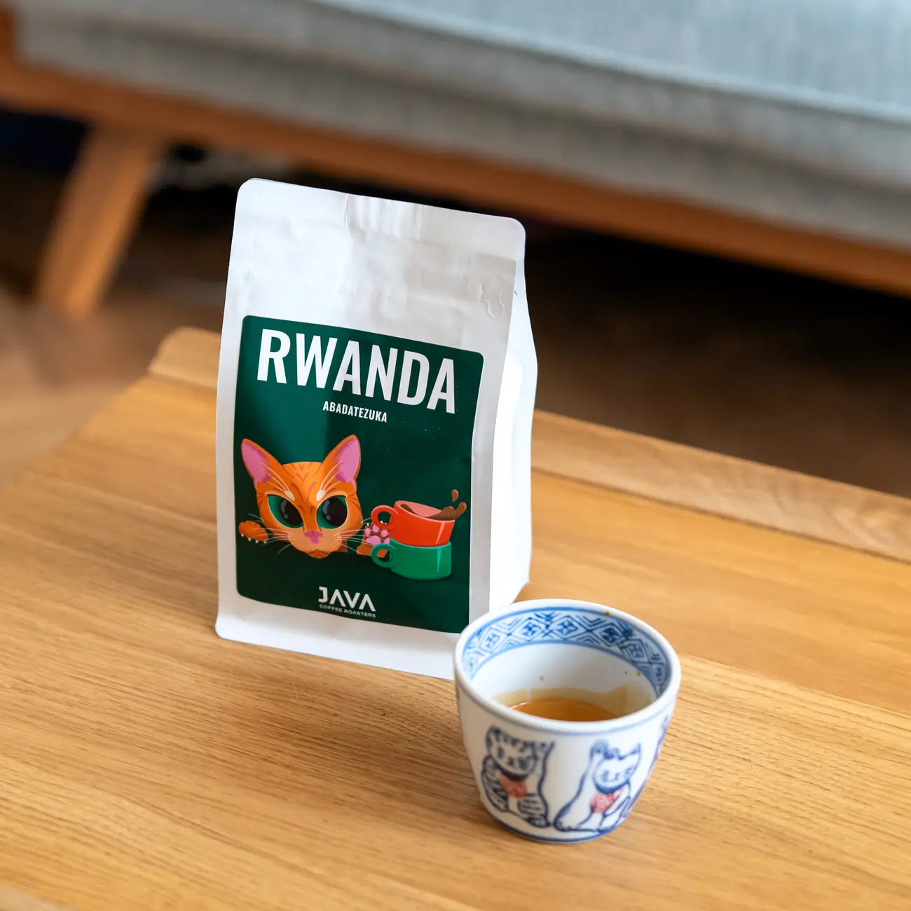 Opakowanie kawy ziarnistej Rwanda Abadatezuka 250 g JAVA Coffee Roasters na stoliku obok filiżanki kawy – oferta B2B
