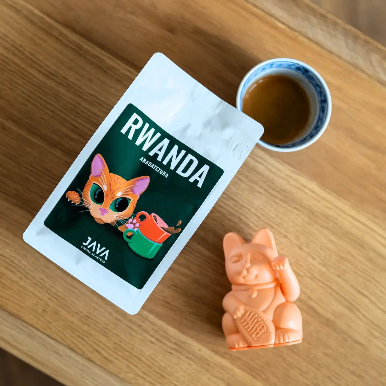 Kawa ziarnista Rwanda Abadatezuka 250 g JAVA Coffee Roasters – specialty Arabica, opakowanie na stoliku obok filiżanki espresso i figurki kota, oferta B2B