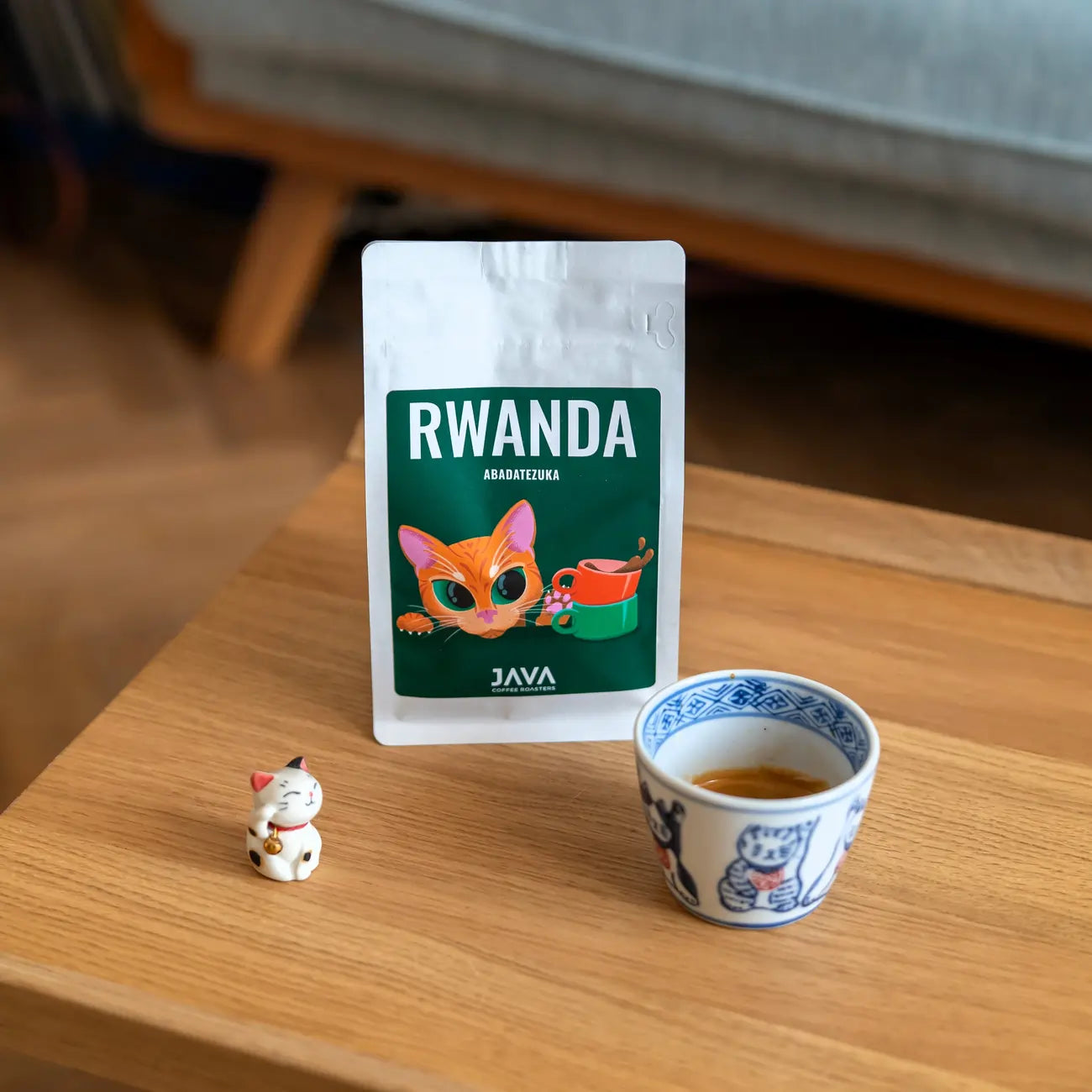 Kawa ziarnista Rwanda Abadatezuka 250 g JAVA Coffee Roasters – specialty Arabica w opakowaniu, na stoliku z filiżanką espresso i figurką kota, oferta B2B