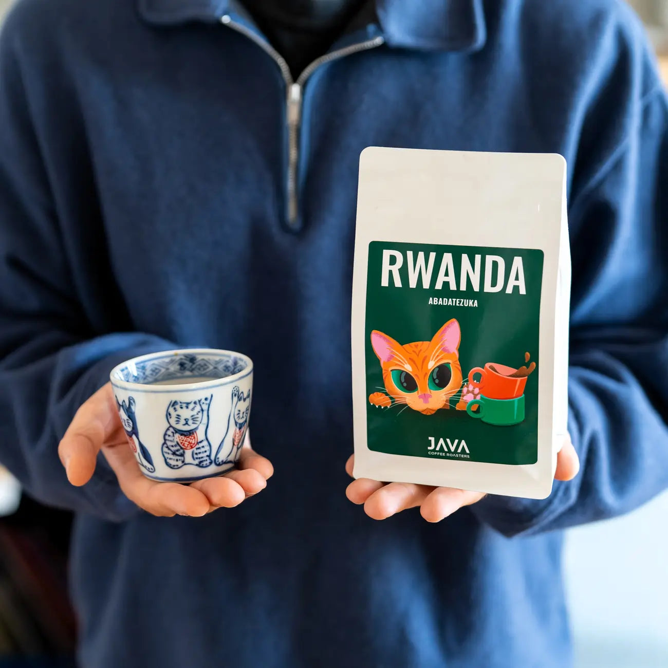Osoba trzymająca kawę ziarnistą Rwanda Abadatezuka 250 g JAVA Coffee Roasters oraz filiżankę kawy – oferta B2B dla biur i gastronomii