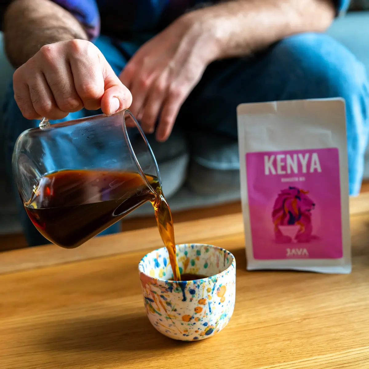 Kawa specialty Kenya Rungeto Kii od JAVA Coffee Roasters – przelewowa kawa nalewana do ceramicznej filiżanki, w tle opakowanie kawy, zdjęcie lifestyle do komunikacji B2B i kawiarni