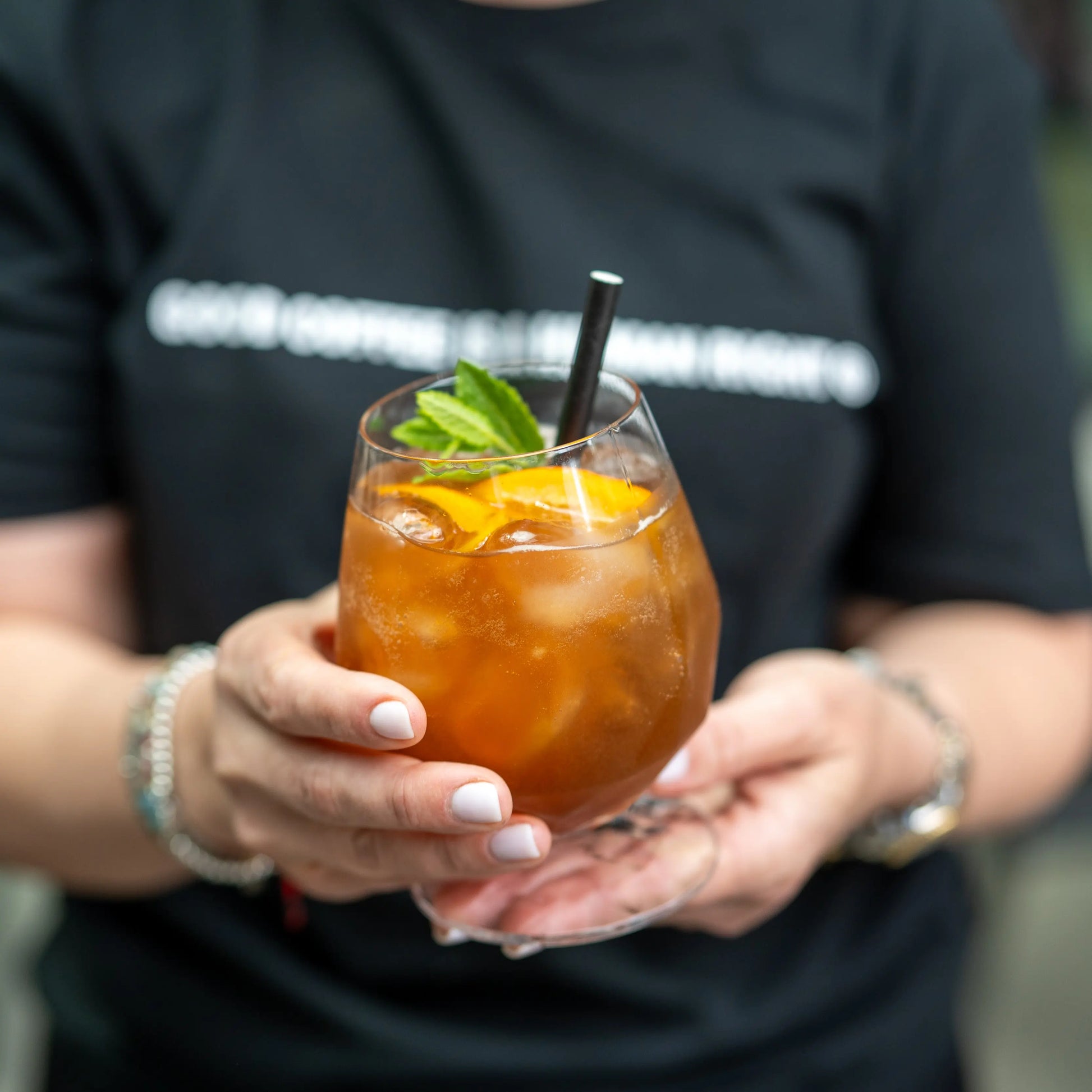 Orzeźwiająca cascara na lodzie z plastrem pomarańczy i miętą – letni napój kawowy w szklance, trzymany w dłoniach od JAVA Coffee Roasters