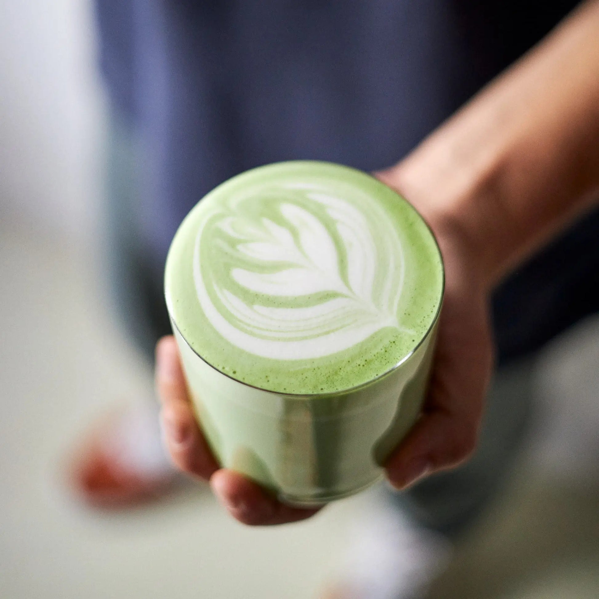 Matcha latte z latte art w filiżance trzymanej w dłoni, kremowa zielona herbata matcha z mlekiem