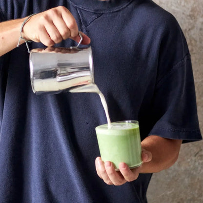 Barista nalewa spienione mleko do matcha latte w szklance, przygotowanie napoju z zielonej herbaty matcha