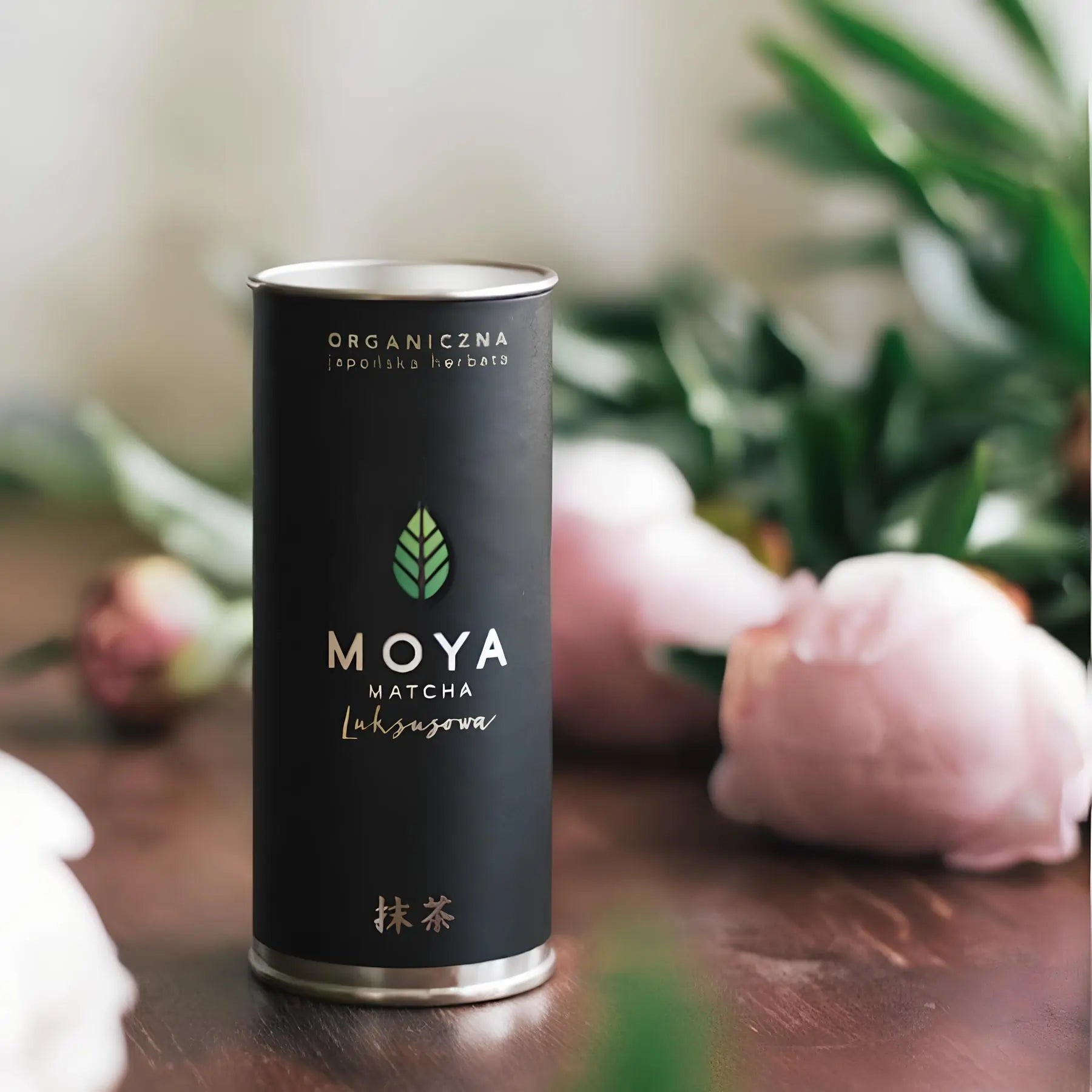  Organiczna japońska herbata matcha MOYA Luksusowa 30g – czarne opakowanie premium na tle kwiatów i liści, zielona herbata w proszku najwyższej jakości